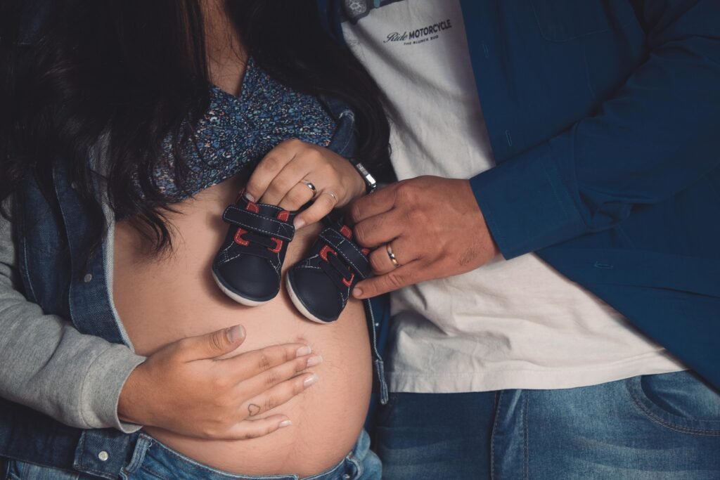 Pregnant couple embracing with baby shoes on belly, symbolizing anticipation and love.