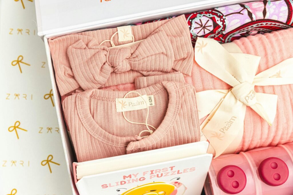pexels-photo-19163668-19163668 Adorable pink baby clothing set with tied bows and a puzzle book in a gift box.