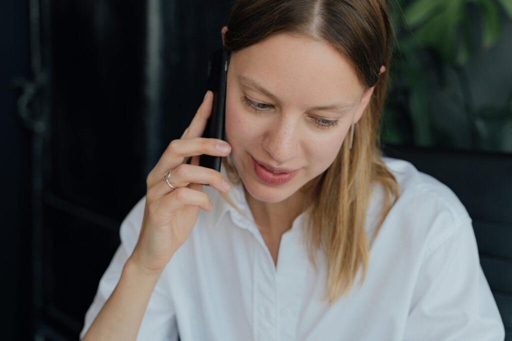 A professional woman in a white shirt making a phone call in an indoor setting, showing communication and business engagement.