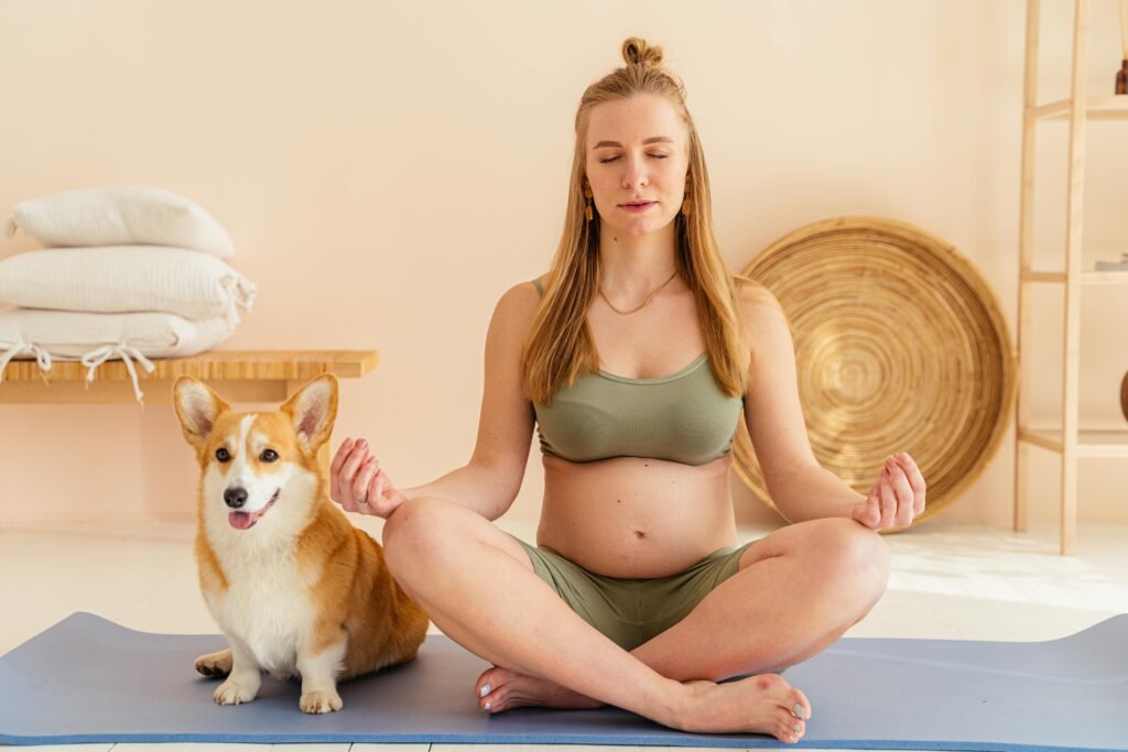 A pregnant woman practices yoga and meditation with her corgi dog indoors, promoting relaxation and mindfulness.
