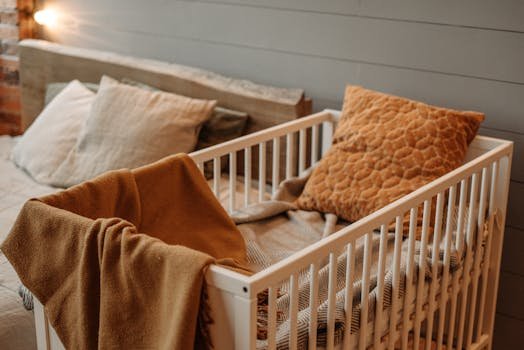 pexels-photo-7937990-7937990 A cozy bedroom featuring a white crib with warm blankets and pillows, creating a comfortable ambiance.